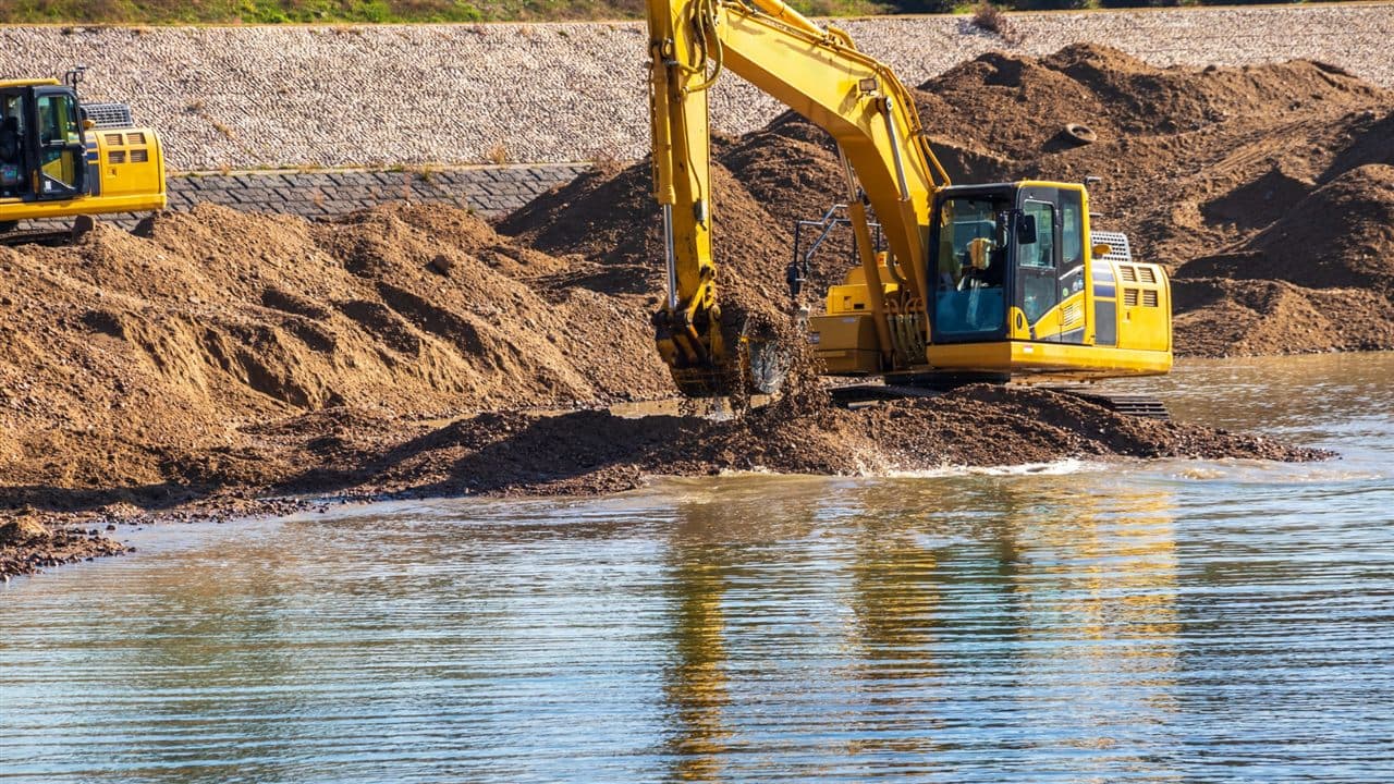 Excavator dredging material along a riverbank
